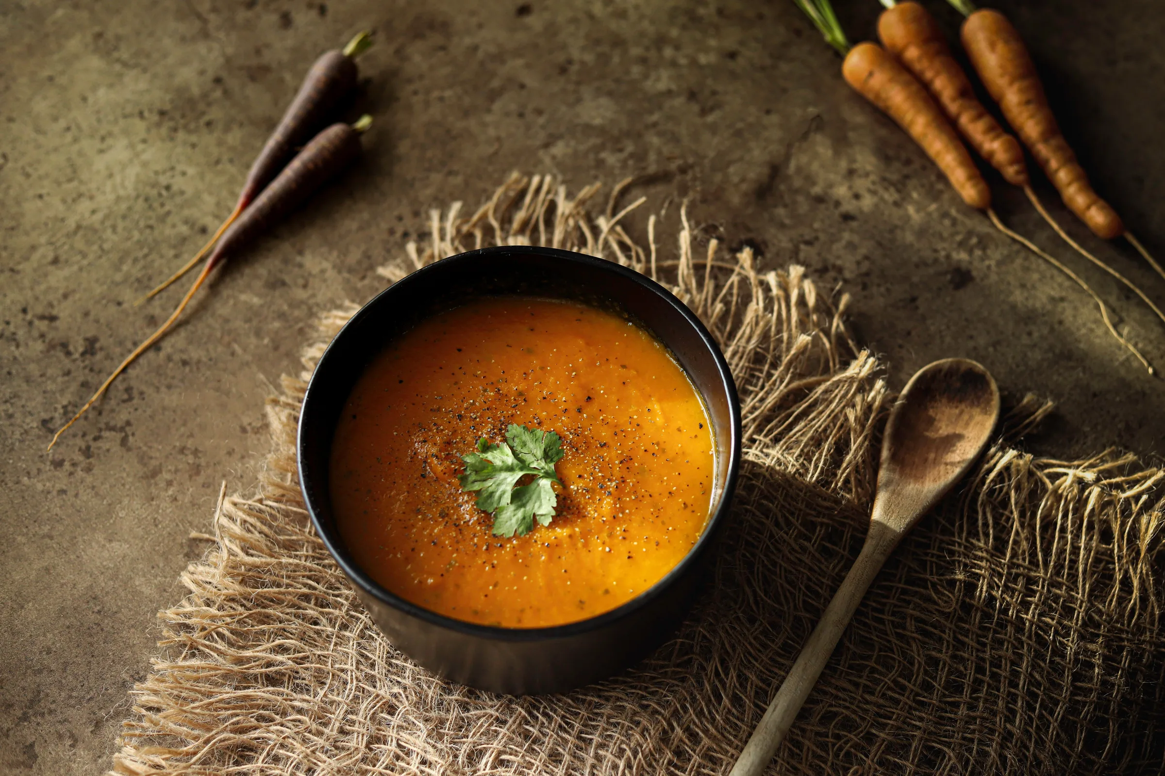 Warm, artisan-styled plant-based carrot soup with fresh carrots on a rustic table