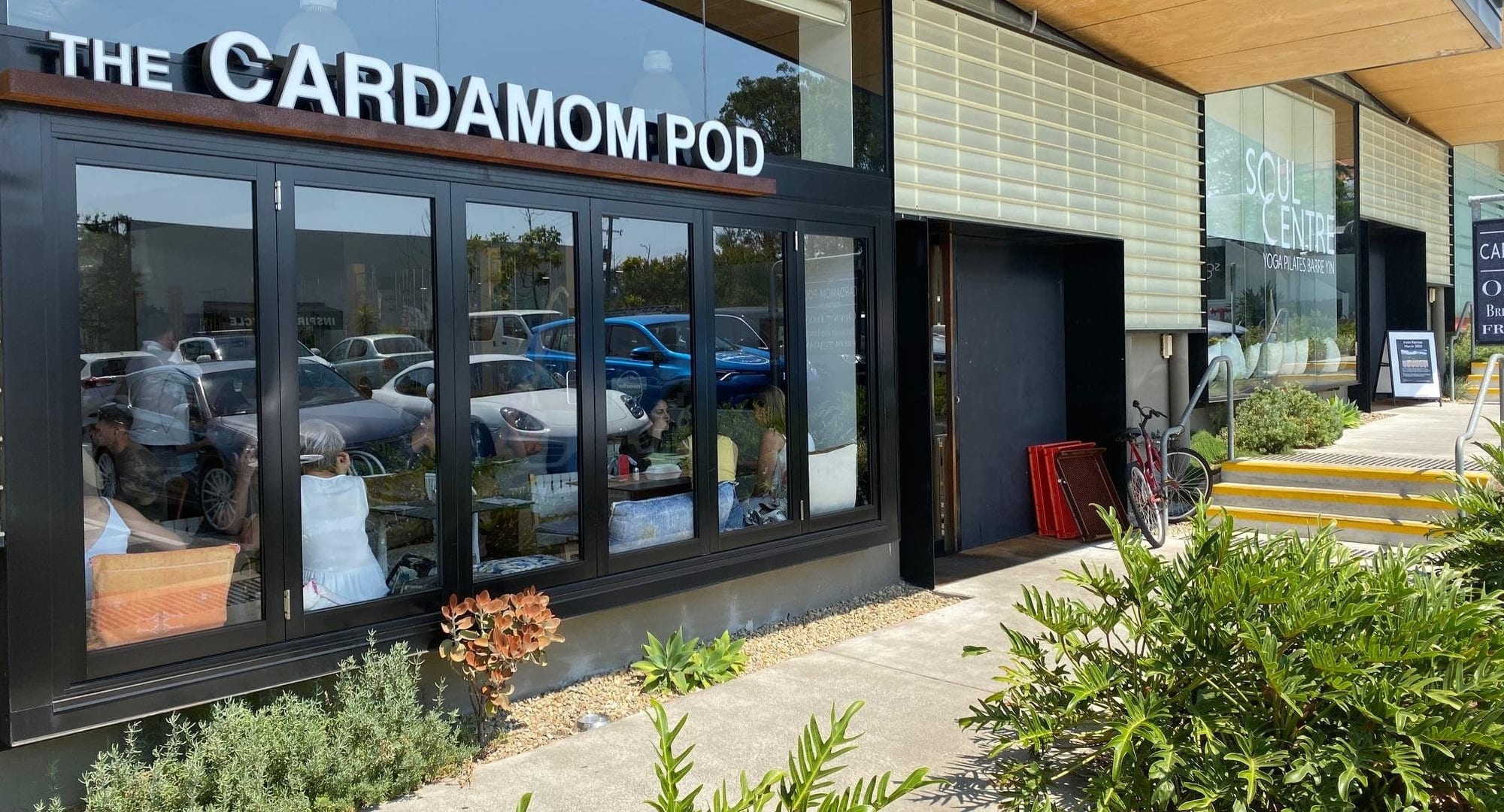 The Cardamom Pod vegetarian cafe storefront at Brickworks, Southport, with signage and glass frontage and diners seated inside