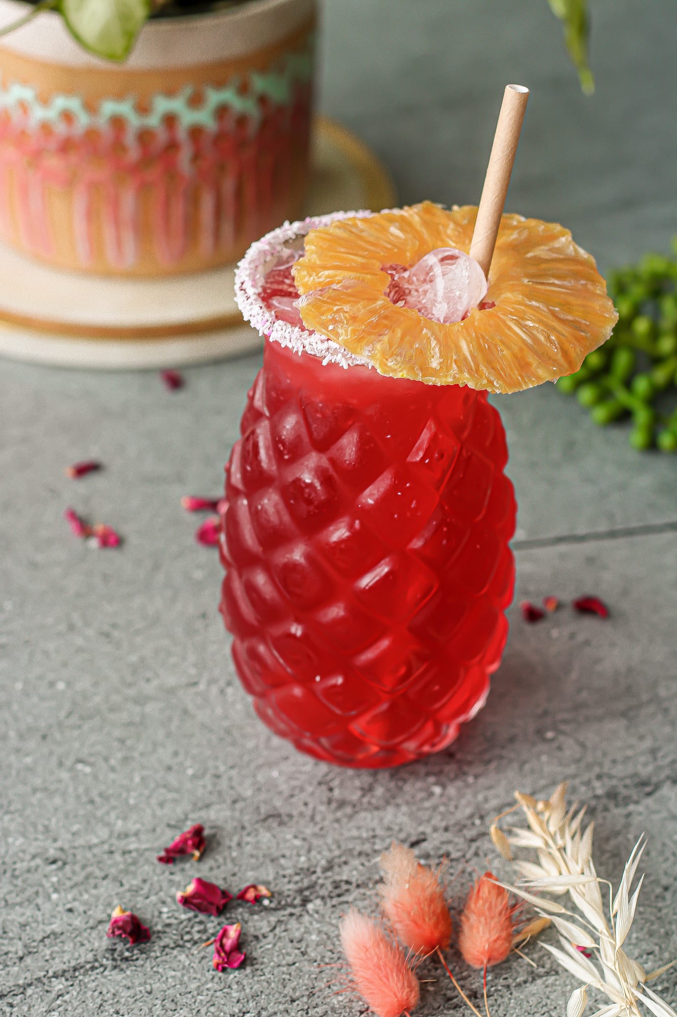Ruby-red tropical cooler in a pineapple-textured glass rimmed with sugar and garnished with dried pineapple