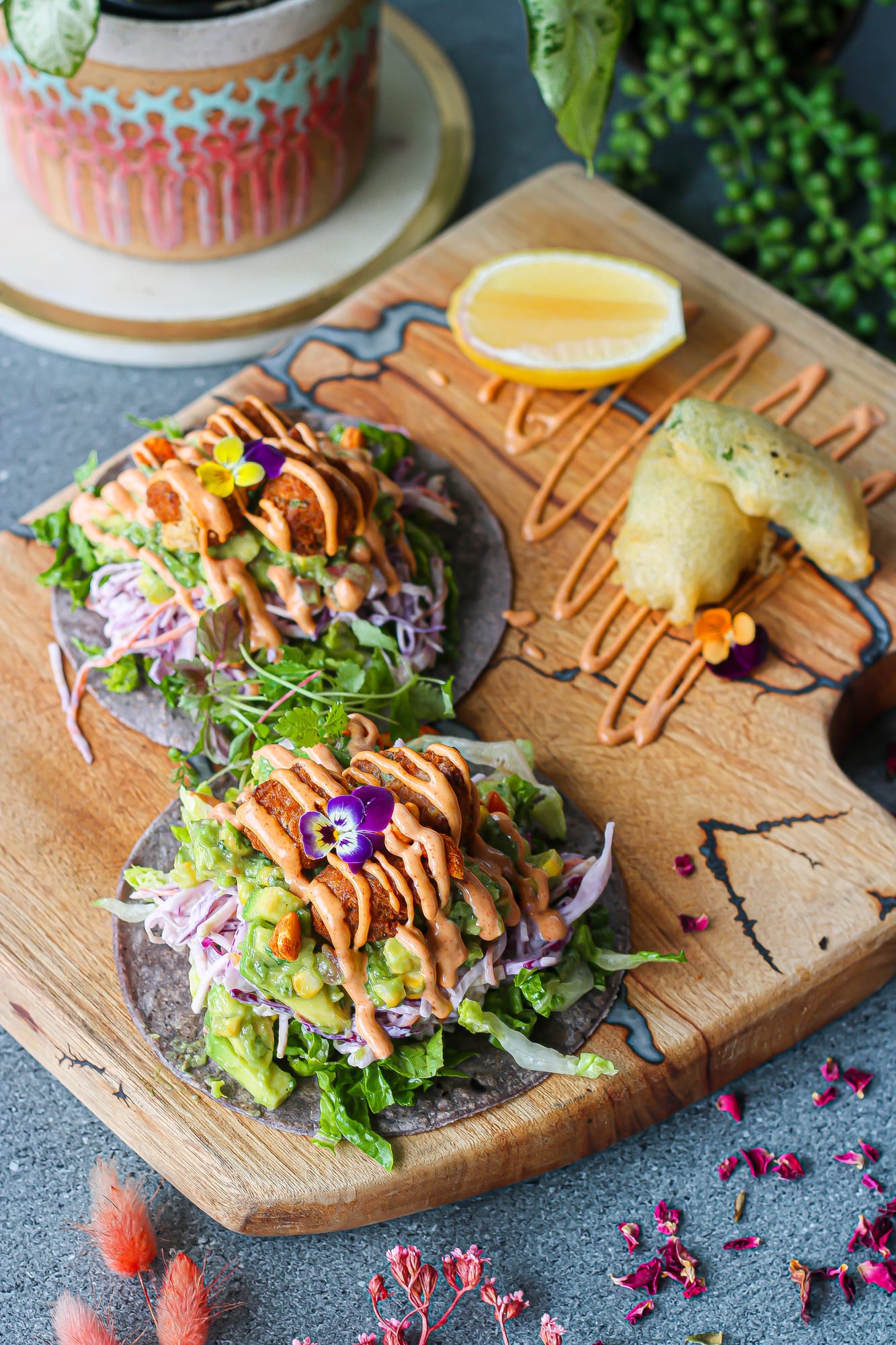 Two vegan tacos on blue-corn tortillas with slaw, guacamole and chipotle drizzle on a wooden board