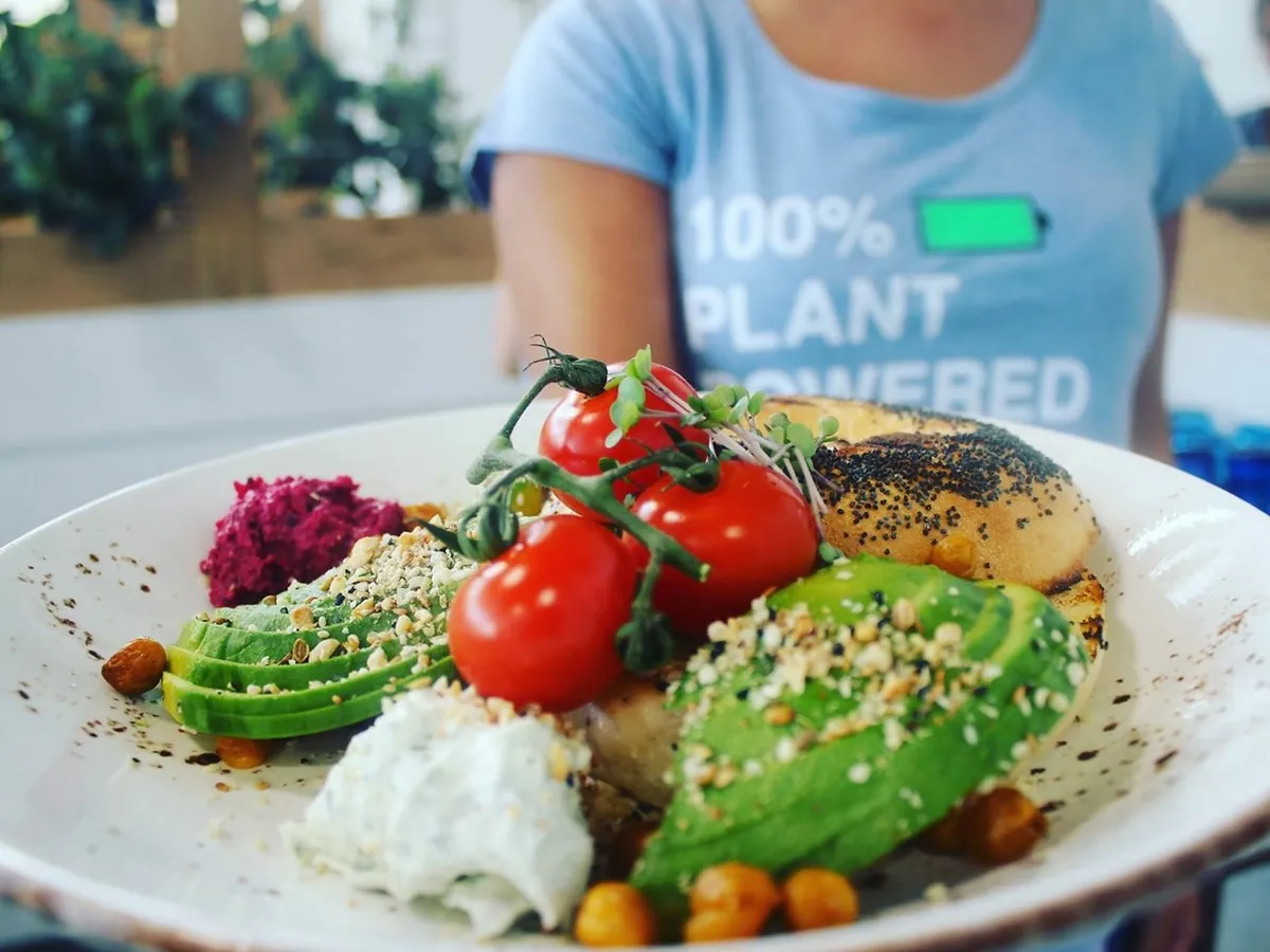 A plant-based breakfast plate with avocado, tomato and dukkah, carried by a member of staff in a 100% Plant Powered shirt