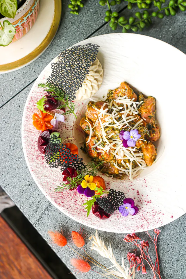 A plated plant-based curry with cashew cream, edible flowers and a sesame tuile