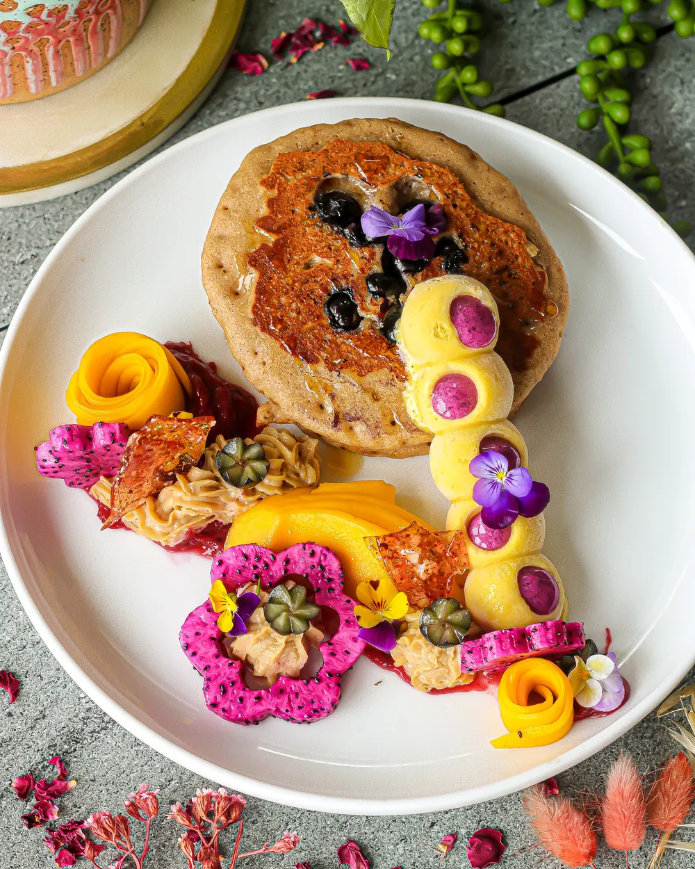 Vegan pancakes plated with mango roses, dragonfruit and edible flowers