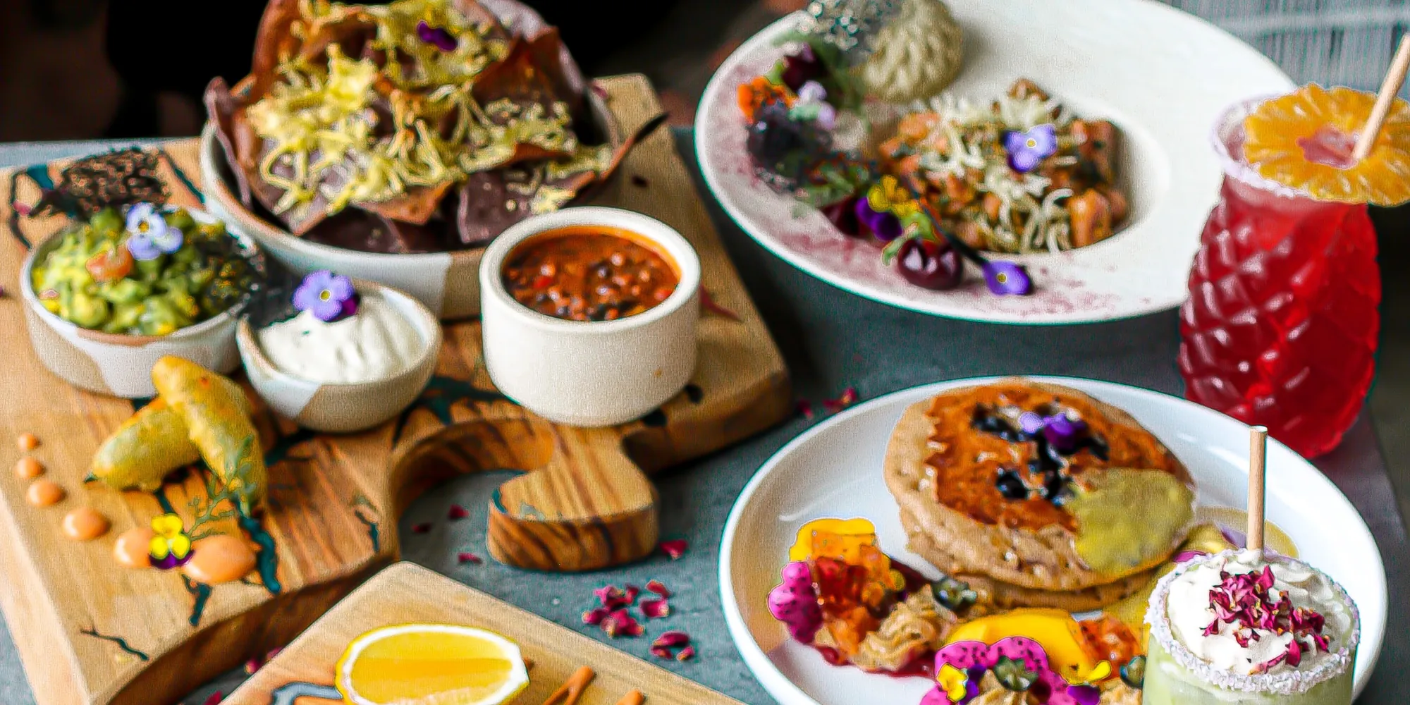 An overhead spread of plant-based dishes, bowls and drinks laid across a shared table at The Cardamom Pod