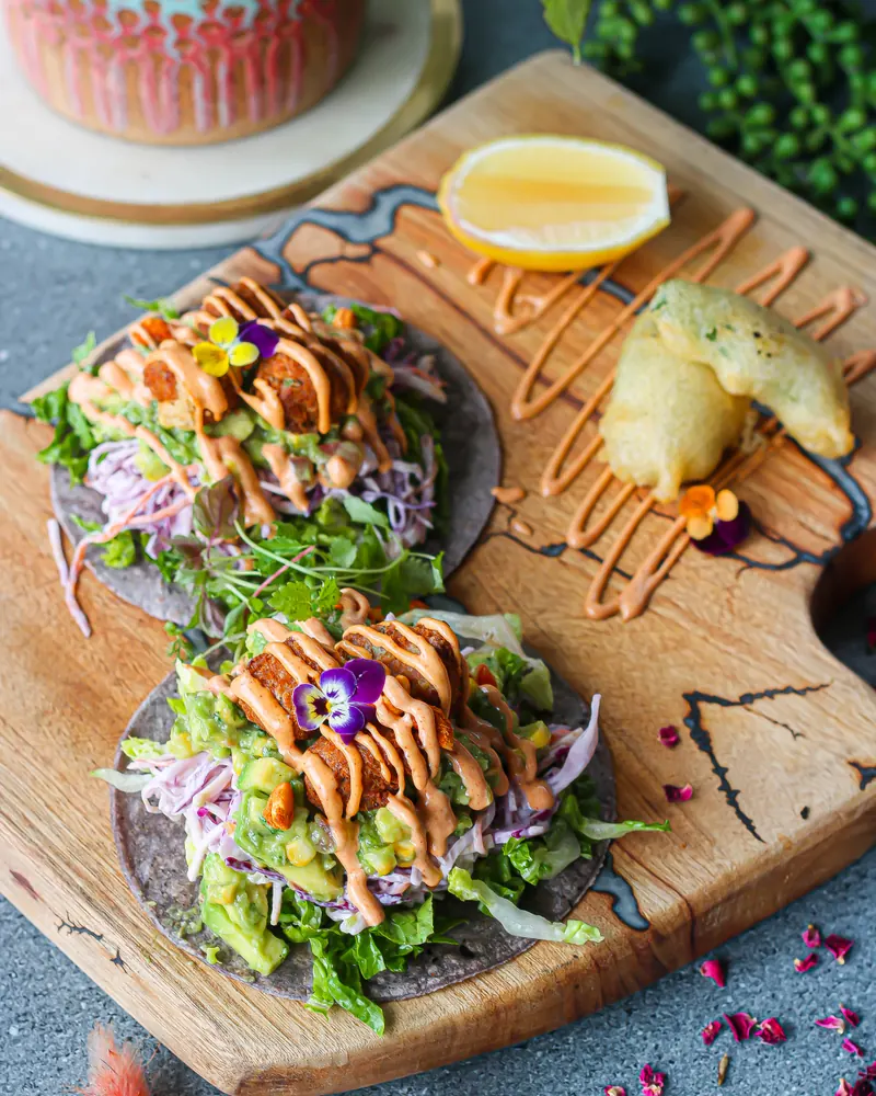 Vegan tacos on blue corn tortillas with slaw, avocado and chipotle sauce on a timber board