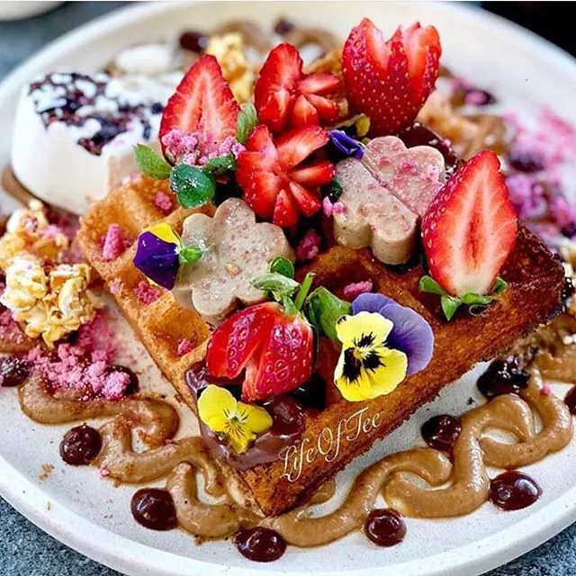 A vegan waffle topped with strawberries, edible flowers and nut butter